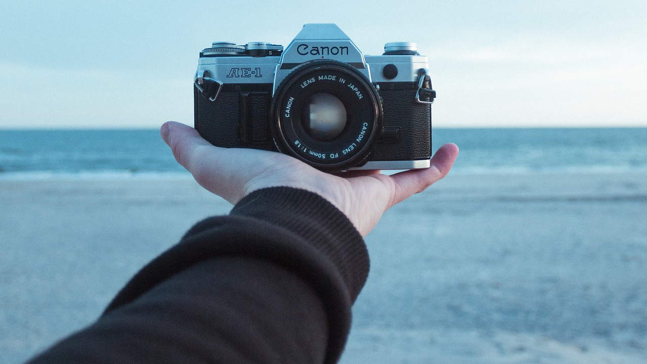 A SLR camera is held in an outstretched hand, but filpped to look back at the photographer.