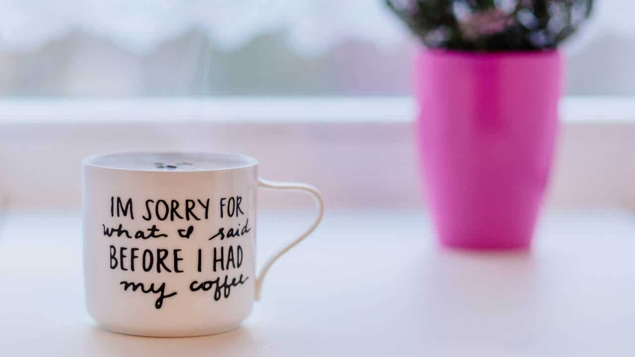 A cup of copy is in the foreground. The text on it reads "Im sorry for what I said before i had my coffee"