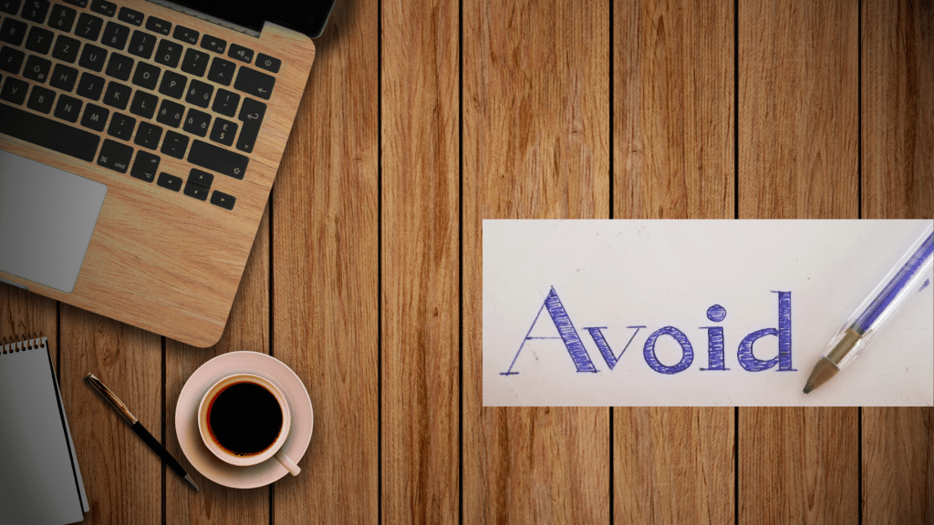 A wooden desk with a laptop, coffee, and a card with the word Avoid written on it